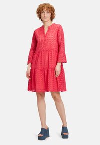 Rotes Augenlochkleid, V-Ausschnitt, dreiviertel Ärmel, gestuftem Rock. Kombiniert mit blauen Plateau-Schuhen. Glatte Textur, dekorative Ausschnitte.