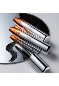 Trois mascaras KIKO Milano dans des tubes argentés à finition brillante, reflétant sur un miroir circulaire, à côté d'un échantillon de mascara noir.