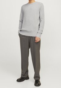 Pull gris clair côtelé avec un col rond, associé à un pantalon gris foncé à fines rayures et des bottes en cuir noir.