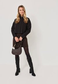 Svart kortärmad skjorta med krage, brun minikjol, svarta knähöga stövlar och en mörkbrun texturerad handväska med detaljer i guld.