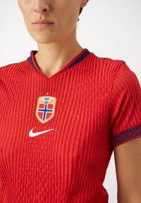 Red soccer jersey with textured vertical patterns, v-neck design, and blue accents. Includes a Norway badge and Nike logo on the chest.