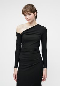 Μαύρο μακρυμάνικο φόρεμα με ασύμμετρη λαιμόκοψη και ραφή με τριμμένα στοιχεία. Φτιαγμένο από ριπ ύφασμα, διαθέτει εφαρμοστό σιλουέτα.