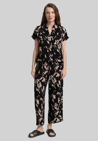 Conjunto de camisa de manga corta con estampado negro y beige y pantalones de pierna ancha, hecho de tela ligera, combinado con sandalias negras tipo deslizante.