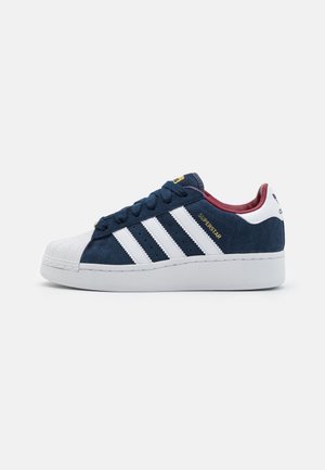 Low-Top Adidas Superstar Sneaker aus marineblauem Veloursleder mit weißer Schalenkappe, weißen Streifen und bordeauxfarbener Innenausstattung, Seitenansicht.