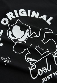 Camiseta negra con un gráfico blanco de un personaje de dibujos animados y el texto "El Gato Cool Original" con "Desde 1919" en una fuente cursiva.