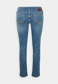 Jeans de ganga azul com corte reto. Apresentam bolsos traseiros com costura amarela e uma etiqueta de marca em pele castanha acima da cinturilha.