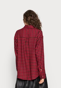 Camicia a quadri rossa e nera con colletto button-down, maniche lunghe e vestibilità rilassata. Presenta un corsetto sul retro e polsini con bottone.