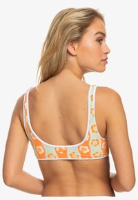 Geribde bralette in lichtgroen met oranje bloemenpatronen. Beschikt over brede bandjes en een afgeronde achterkant met witte randafwerking.