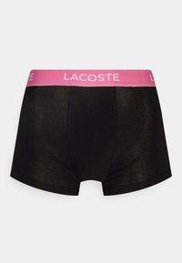 Fekete boxer alsónadrág széles rózsaszín derékpánttal, amelyen a "LACOSTE" logó található. Sima textúra, varrási kiemelések és szoros illeszkedés jellemzi.