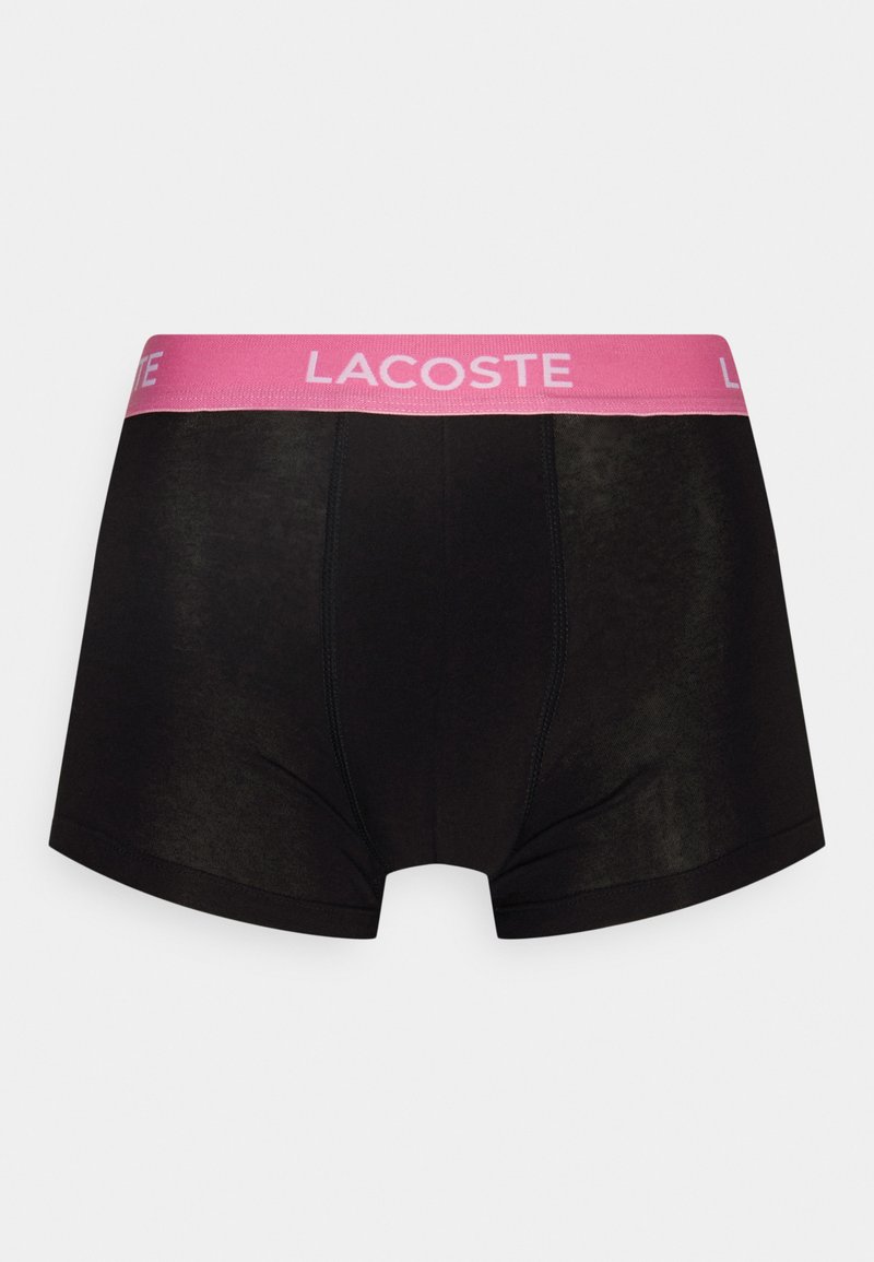 Zwarte boxershorts met een brede roze tailleband waarop het "LACOSTE" logo staat. Glad textuur met stiksels en een snug fit.