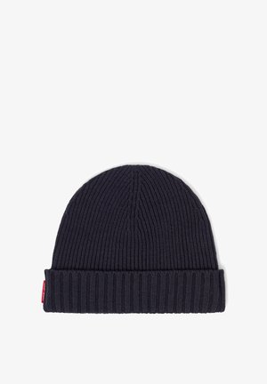 Navy blue knitted beanie hat with vertical ribbing and a folded cuff, featuring a small red logo tag on the side.