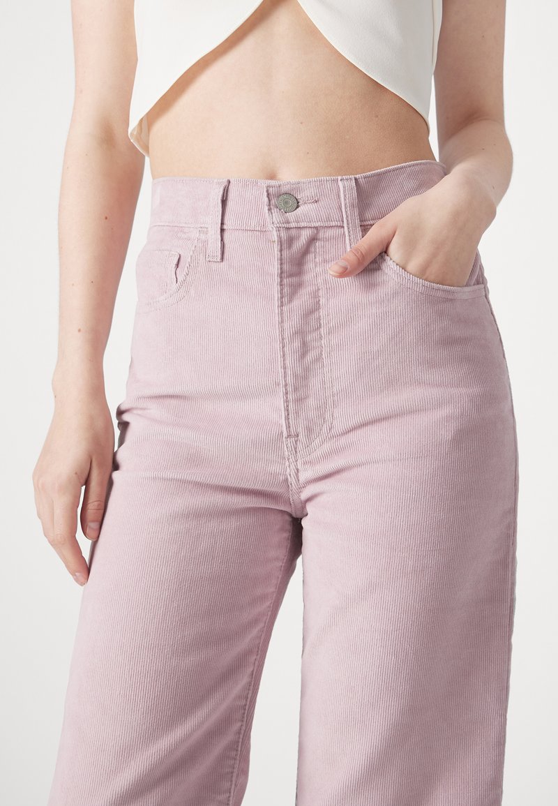 Pantalons en velours côtelé rose avec une taille haute, coupe droite et poches latérales. Présentent une texture rayée verticale et une fermeture à bouton en métal.
