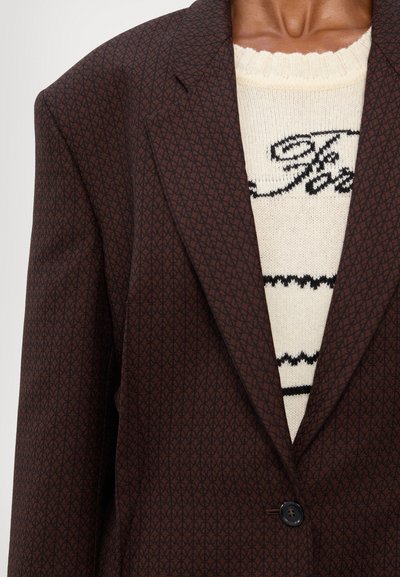 Pruun mustriga bleiser teravate läbiltidega, ühekordse nööbi sulgemisega, koos kreemika kudumiga, millel on must kiri ja triibud.