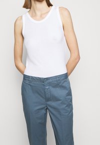 Top sin mangas blanco de algodón, combinado con pantalones de algodón azul claro que tienen un botón y una etiqueta sutil en la cinturilla.