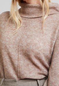 Neuledekorin turtleneck-pusero pehmeässä beigevärissä, jossa on hienovarainen tekstuuri ja rento istuvuus saumattomalla muotoilulla.