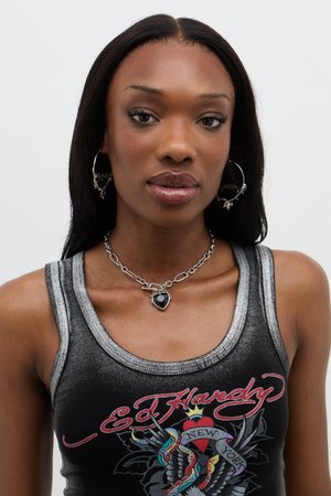 Black tank top with gray accents, featuring a graphic design. Silver hoop earrings and a necklace with a black heart pendant complete the look.