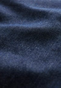Marineblauer Stoff mit feiner Textur, eng gewebten Fäden und leichtem Glanz, der subtile Wellen und Falten aufweist.