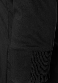 Black shirt fabric with a textured, gathered cuff detail. Smooth texture with a clean seam finish. Simple design without additional patterns.