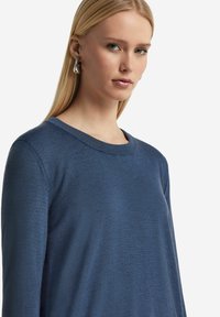 Wielki sweter z długim rękawem i okrągłym dekoltem w głębokim granatowym kolorze. Wykonany z miękkiej, teksturowanej tkaniny. Posiada luźny krój i ściągacz w dekolcie.