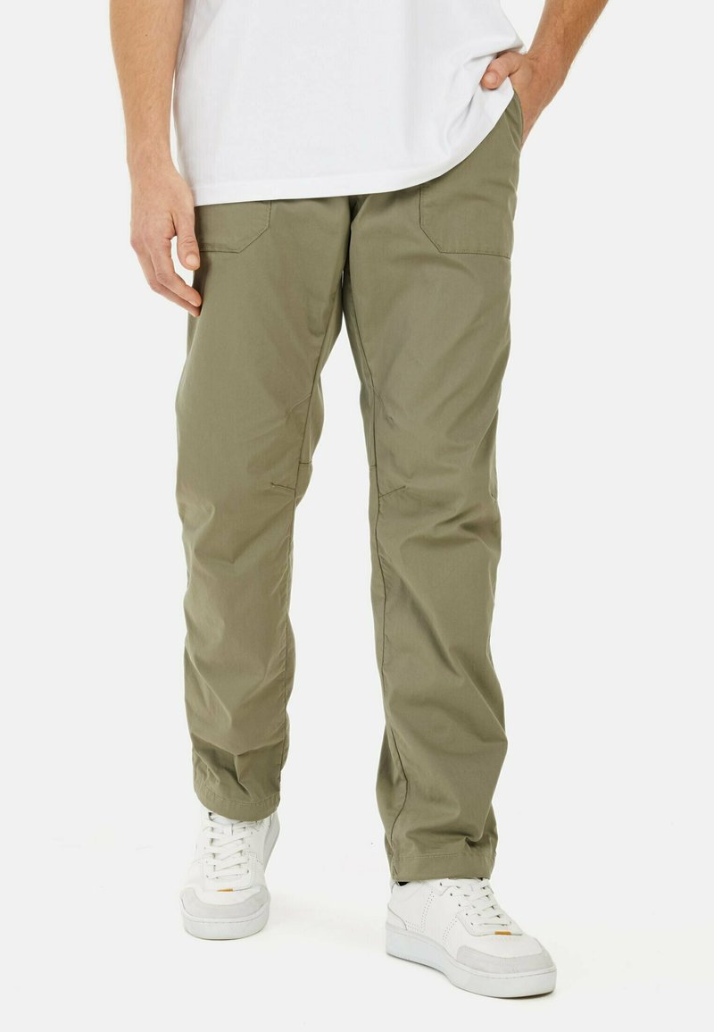 Pantalons cargo vert olive en tissu léger, avec poches latérales, coupe slim et jambes fuselées, associés à des baskets blanches.