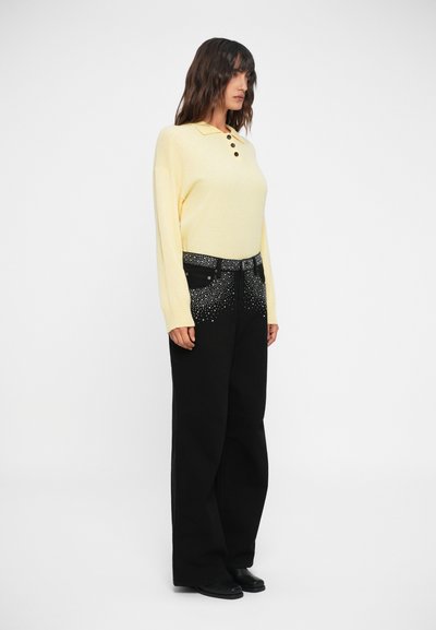 Long-sleeve yellow polo with three buttons, paired with wide-leg black jeans featuring a gradient of metallic studs on the front.