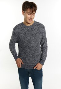 Mėlynos ir baltos spalvų megztinis, su apykakle, tekstūruotas raštas, ilgos rankovės ir šonkaulio kantas; dėvimas su mėlynomis džinsomis.