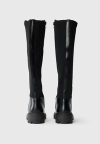 Bottes noires à mi-mollet présentant un design élégant avec une base en cuir lisse et un haut en textile extensible, accentuées par des panneaux latéraux brillants.