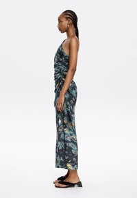 Sleeveless, ruched dress in dark, patterned fabric featuring seashell and botanical motifs. Paired with black sandals with textured accents.
