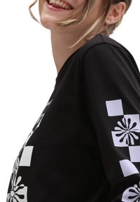 Schwarz langärmliges Shirt mit weißen Blumen- und geometrischen Mustern auf den Ärmeln und der Vorderseite, aus einem weichen, strukturierten Stoff.