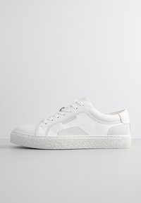 Zapatillas blancas con parte superior de cuero suave, panel lateral texturizado y suela de goma con un acabado moteado. Diseño con cordones y detalle de marca.