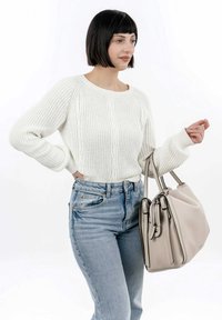 Pull en tricot crème avec un motif en relief, coupe décontractée, associé à un jean taille haute en denim clair. Sac à main beige avec une finition texturée et des accessoires en argent.