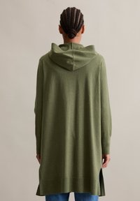 Cardigan long olive avec capuche, en tissu doux, avec des poignets et un ourlet côtelés, fentes latérales pour plus de liberté de mouvement.