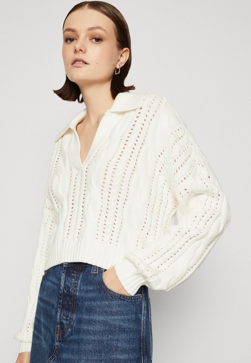 Maglione bianco lavorato a maglia con colletto, motivo a treccia testurizzato e orlo a coste. Abbina a jeans blu scuro, mostrando un look casual.