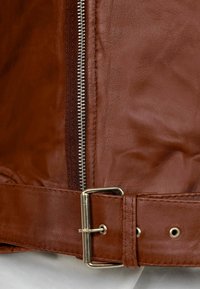 Giacca di pelle marrone con zip argentata, cintura in vita con fibbia metallica e texture liscia con un leggero riflesso.