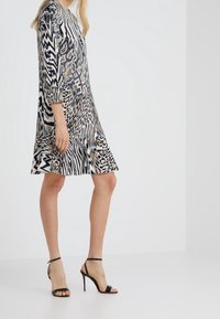 Svartvit mönstrad klänning med leoparddetaljer, långa ärmar, utsvängd nederdel, bärs med svarta högklackade sandaler. Slät tygtextur.