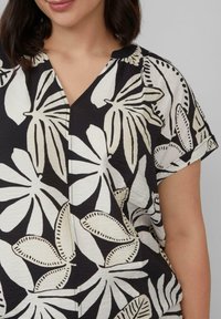 Kurzärmliges Oberteil mit einem schwarz-weißen Blumenmuster, V-Ausschnitt und strukturiertem Stoff mit kontrastierenden Blattmustern.