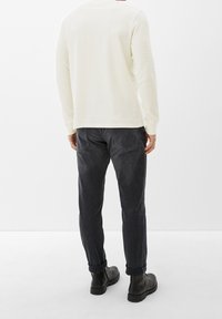 Pullover a maniche lunghe di colore crema con tessuto texturizzato abbinato a pantaloni grigi scuri. Chi lo indossa ha anche stivali neri alla caviglia. Design semplice e minimalista.