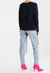 Cardigan lavorato a maglia navy con scollo rotondo e bottoni sul retro, abbinato a jeans azzurri chiari e stivali con tacco alla caviglia di un vivace colore rosa.
