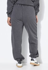 Grijze sweatpants met elastische boorden, relaxed fit, zachte textuur en een tailleband met trekkoord. Gecombineerd met witte sneakers met zwarte accenten.