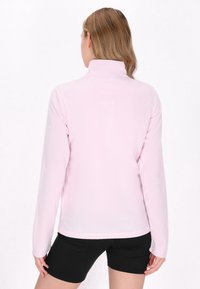 Lyserød langærmet fleece-pullover med høj krave og glat tekstur, parret med sorte shorts. Bagudsigten viser minimale syninger.