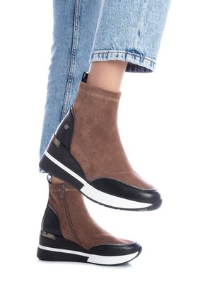 Botas altas de ante marrón con acentos negros, suela blanca y cremallera lateral. La superficie texturizada y los detalles lisos contrastan en el diseño.