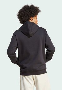 Felpa nera in cotone con cappuccio, cuciture a vista e vestibilità comoda. Presenta una texture morbida e polsini e orlo a costine.
