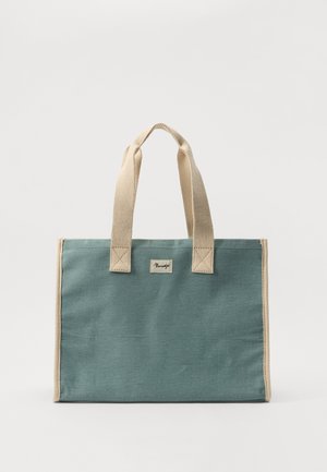 Drobėtos rankinės nuošalyje melsva spalva su smėlio spalvos rankenomis, turinti mažą logotipo etiketę ir kvadratinę formą. Tekstūruota medžiaga, sustiprinti siūlės.