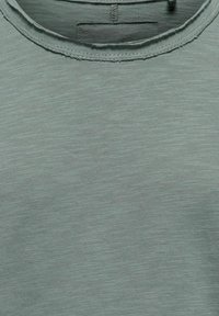 Jasnozielona koszulka z miękkiego, teksturowanego materiału. Posiada okrągły dekolt oraz widoczne szwy wzdłuż kołnierza i dołu.