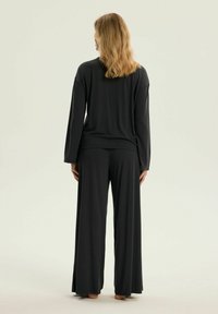 Czarny top z długim rękawem zestawiony z szerokimi spodniami o luźnym kroju, oba wykonane z gładkiej tkaniny. Ubranie ma luźny fason i prosty design.