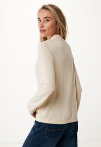 Beige lättviktig tröja med långa ärmar, rund halsringning och en mjuk textur, tillsammans med mörkblå jeans med bakfickor.