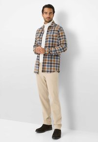 Camicia a quadri in tonalità di marrone e blu, con due tasche sul petto. Abbinata a pantaloni beige chiaro e stivali marrone scuro. Tessuto morbido.