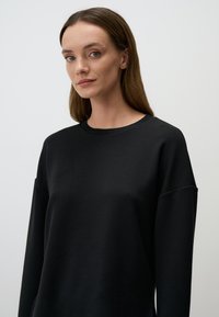 Felpa nera realizzata in tessuto morbido, caratterizzata da un collo rotondo, vestibilità ampia e spalle scese. Texture liscia con dettagli di design minimi.