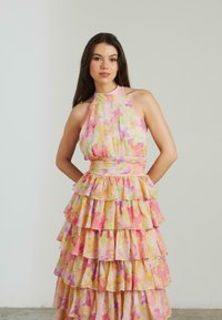 Abito a balze floreale in tonalità pastello di rosa, giallo e verde, con scollatura a halter e strati arricciati per un aspetto testurizzato.
