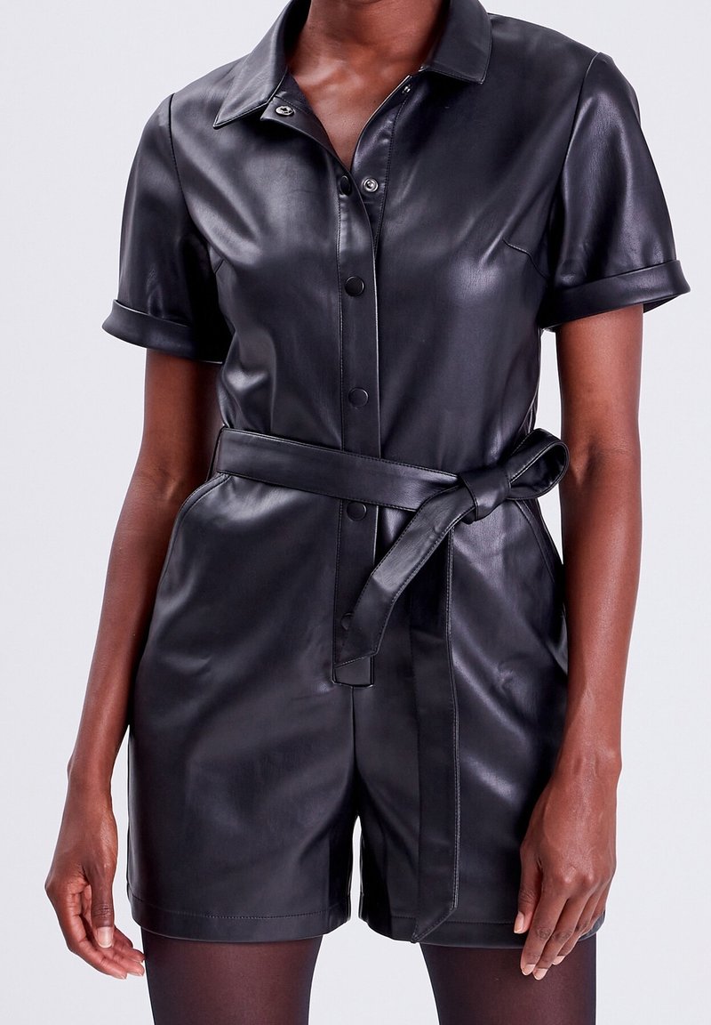 Combinaison noire en cuir avec manches courtes, col et taille ceinturée. Dotée de boutons-pression et d'une texture lisse.